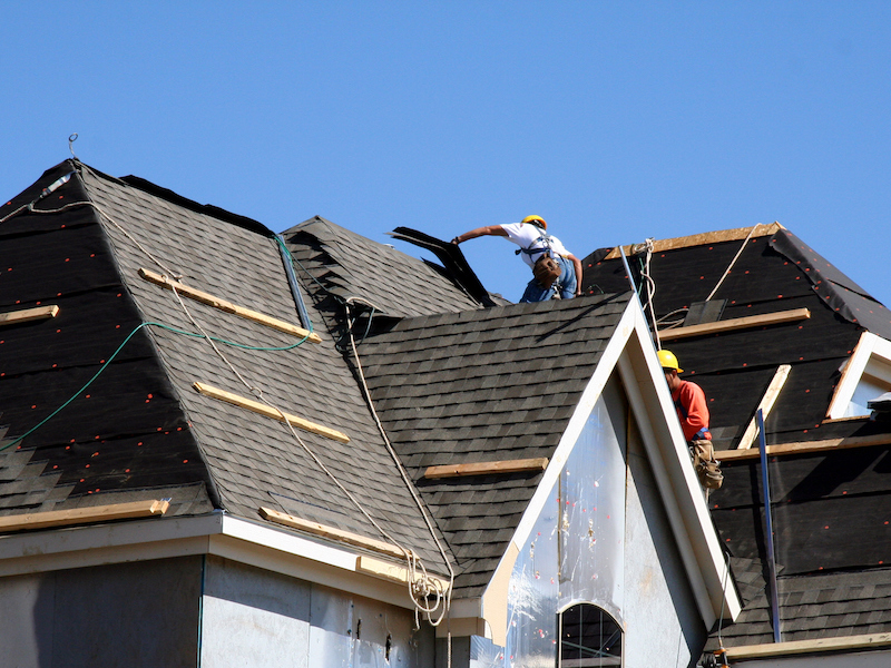 Construction workers putting shingles on the roof of a house.